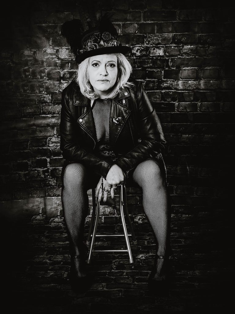 woman in leather jacket against a brick wall posing for the 50 over 50 project boudoir shoot