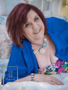 mature woman wearing a blue shirt lying on a bed for boudoir photograph for the 50 over 50 project