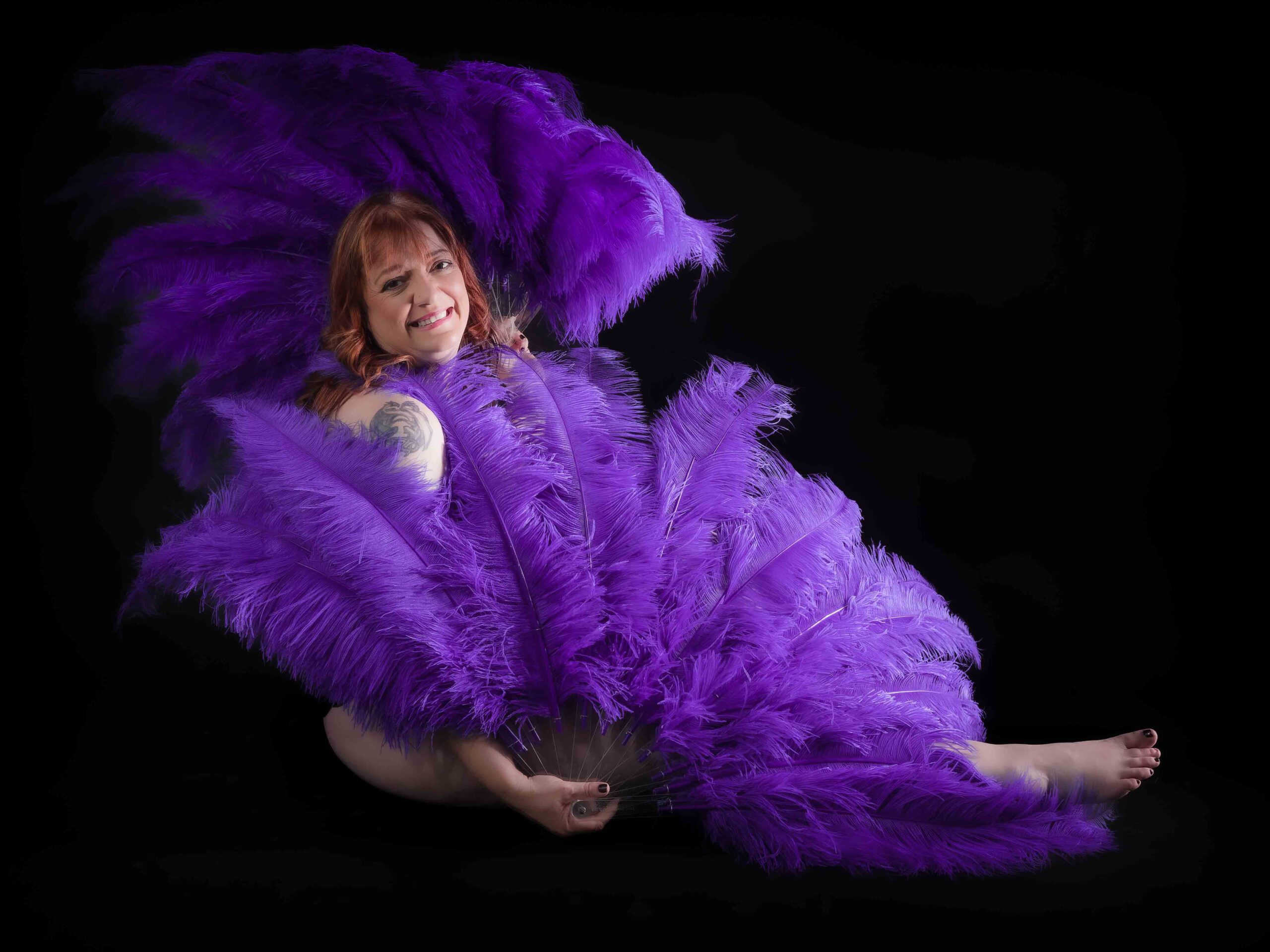 mature woman from the 50 over 50 project sitting on floor with purple feathers