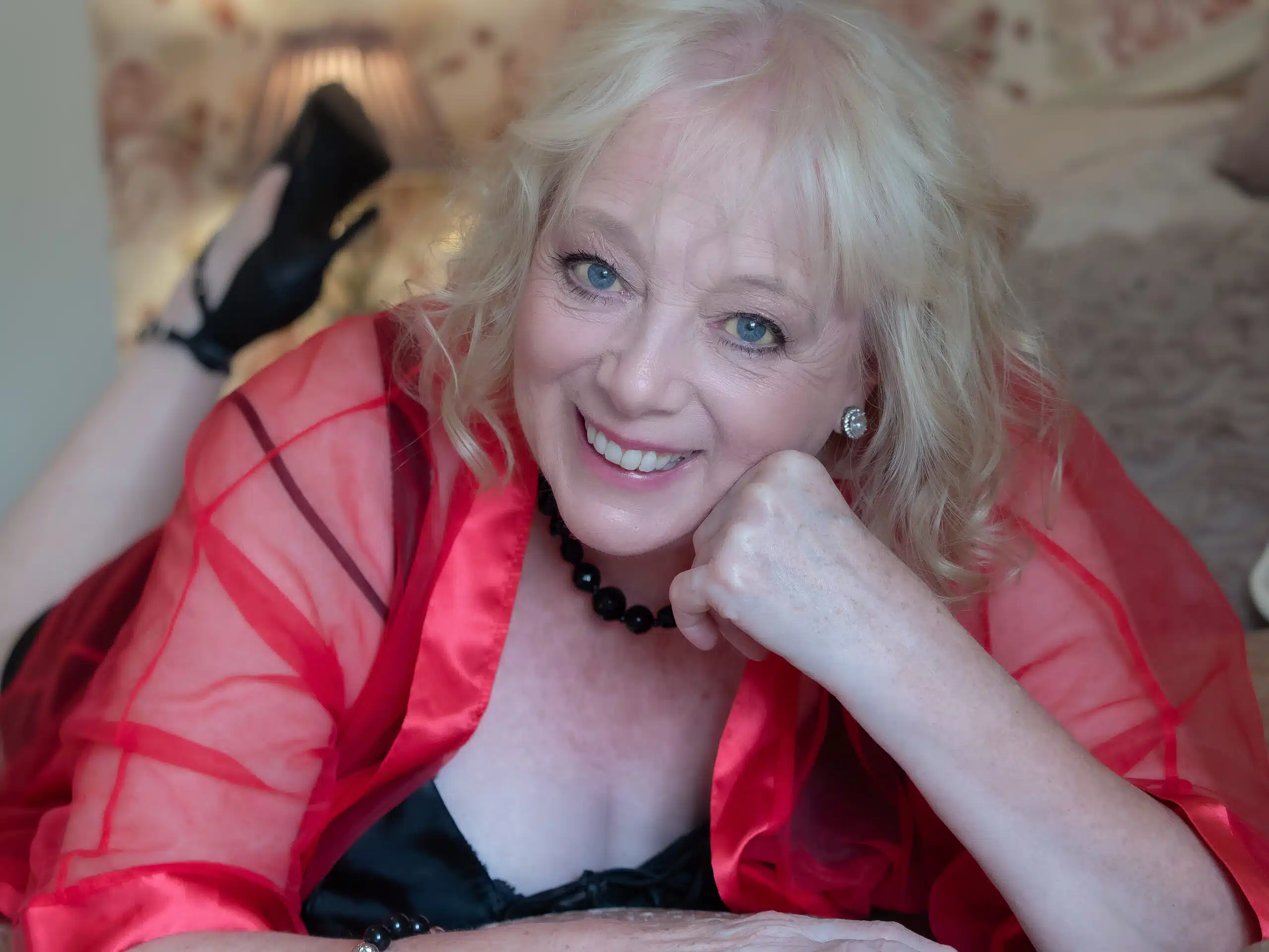 mature woman lying on bed in red robe for the 50 over 50 project