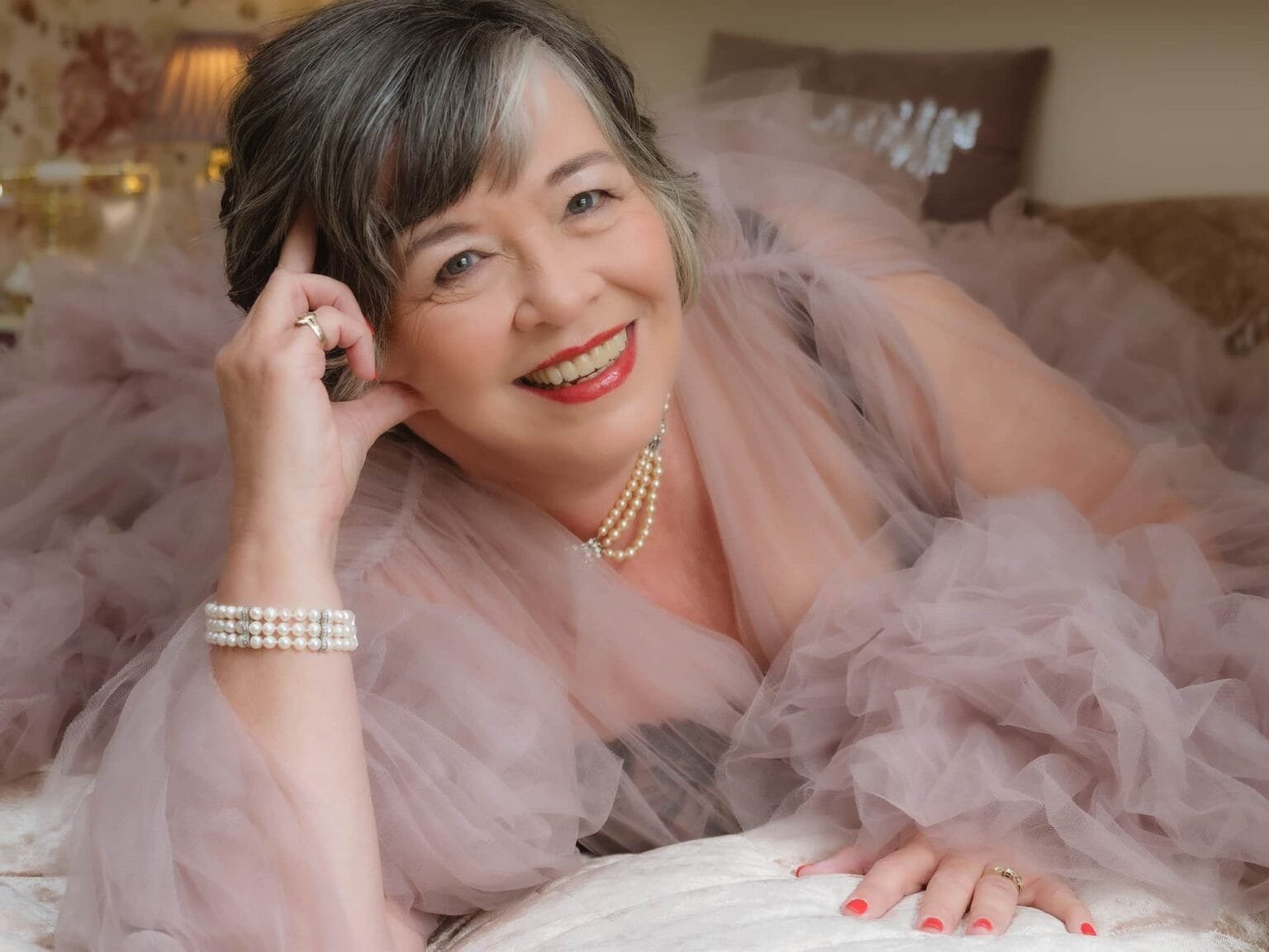 mature woman having a boudoir shoot by Symply Boudoir. Lying on bed with a beautiful pink fothy tulle gown
